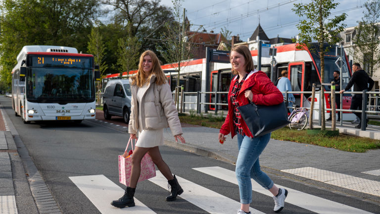 Reizigers naast tramhalte Reigers steken de straat over naast HTM tramhalte