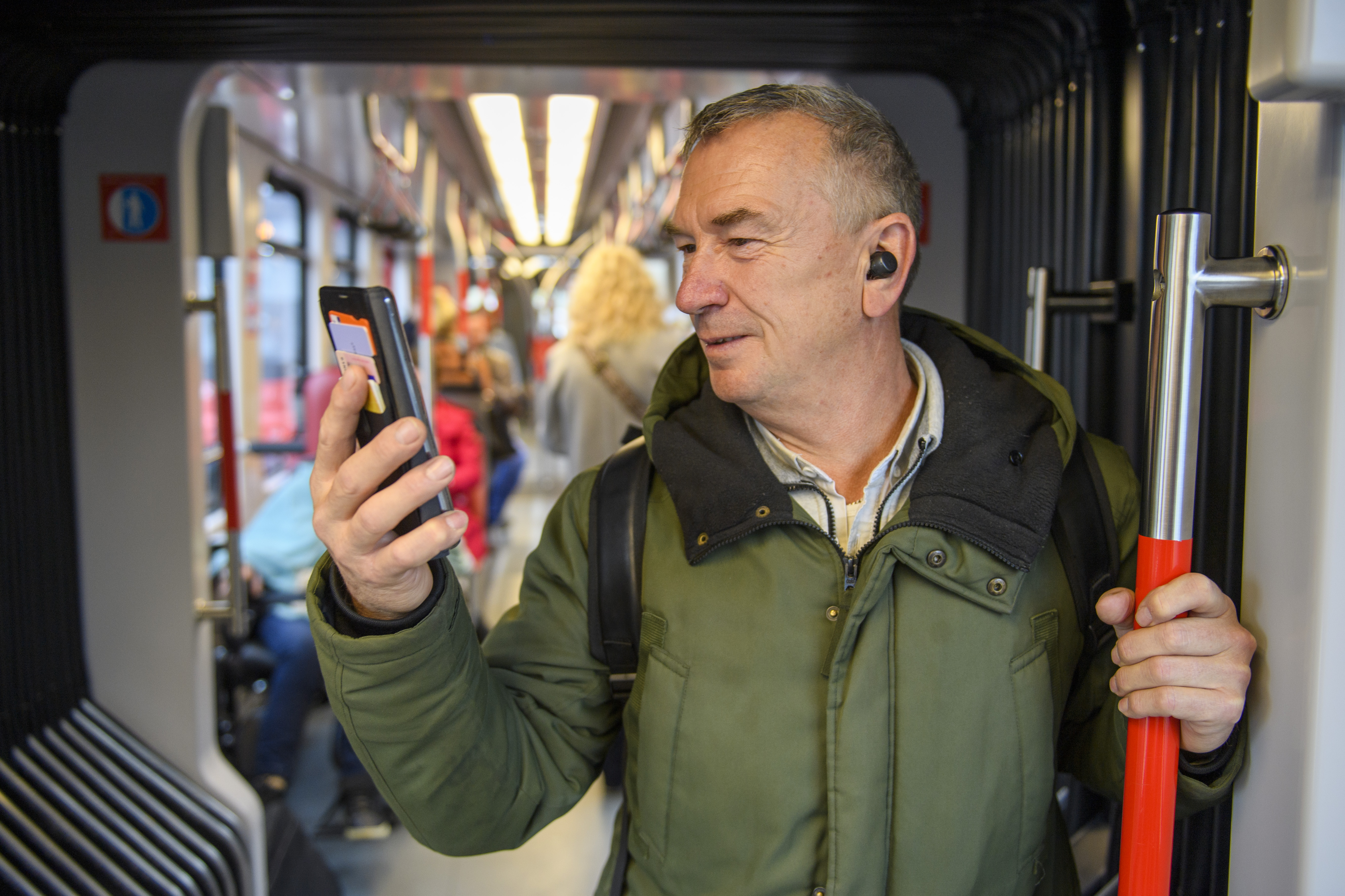 Man staat in HTM tram en kijkt lachend op zijn telefoon