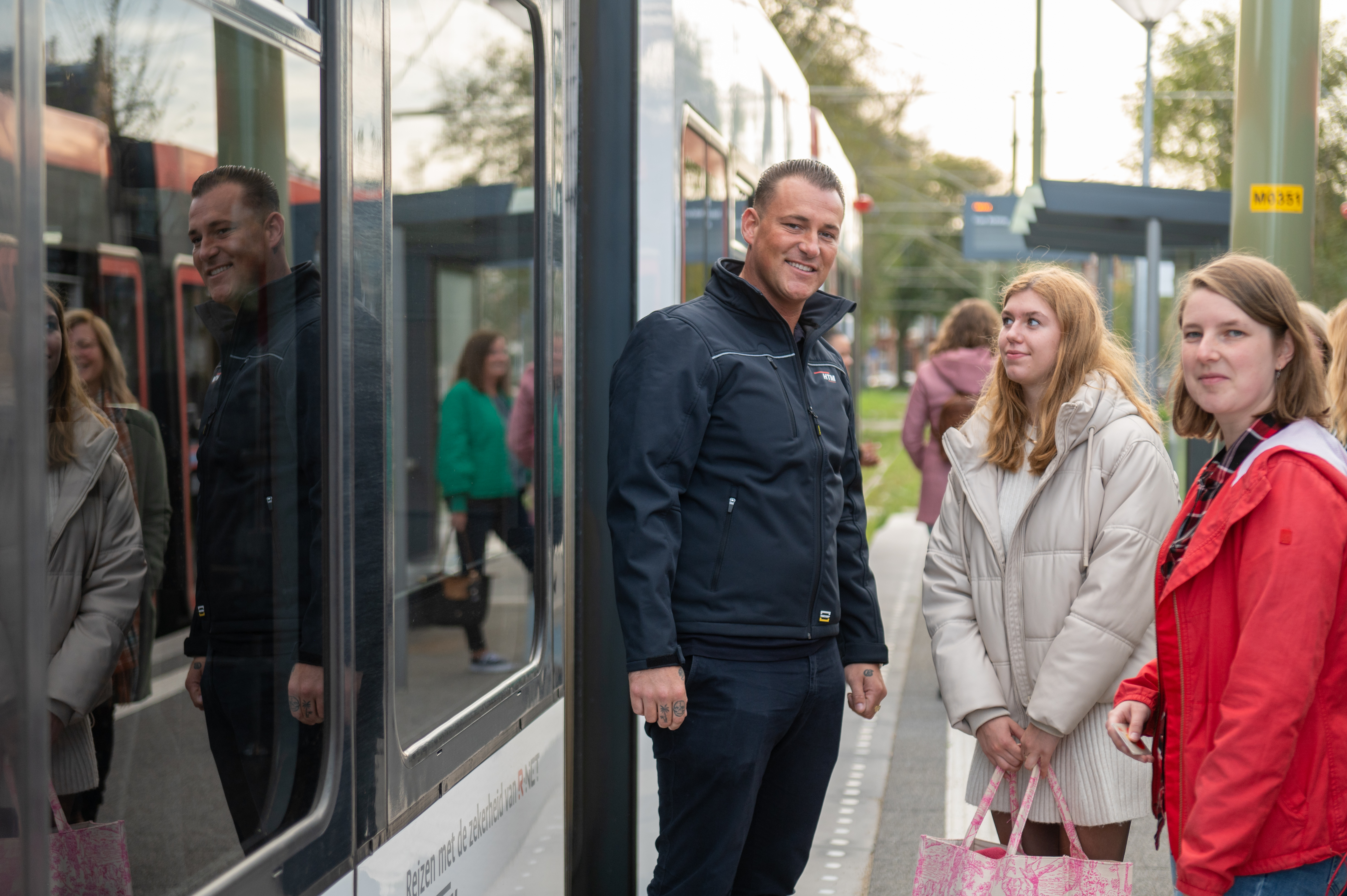 HTM controleur met 2 reizigers naast HTM tram