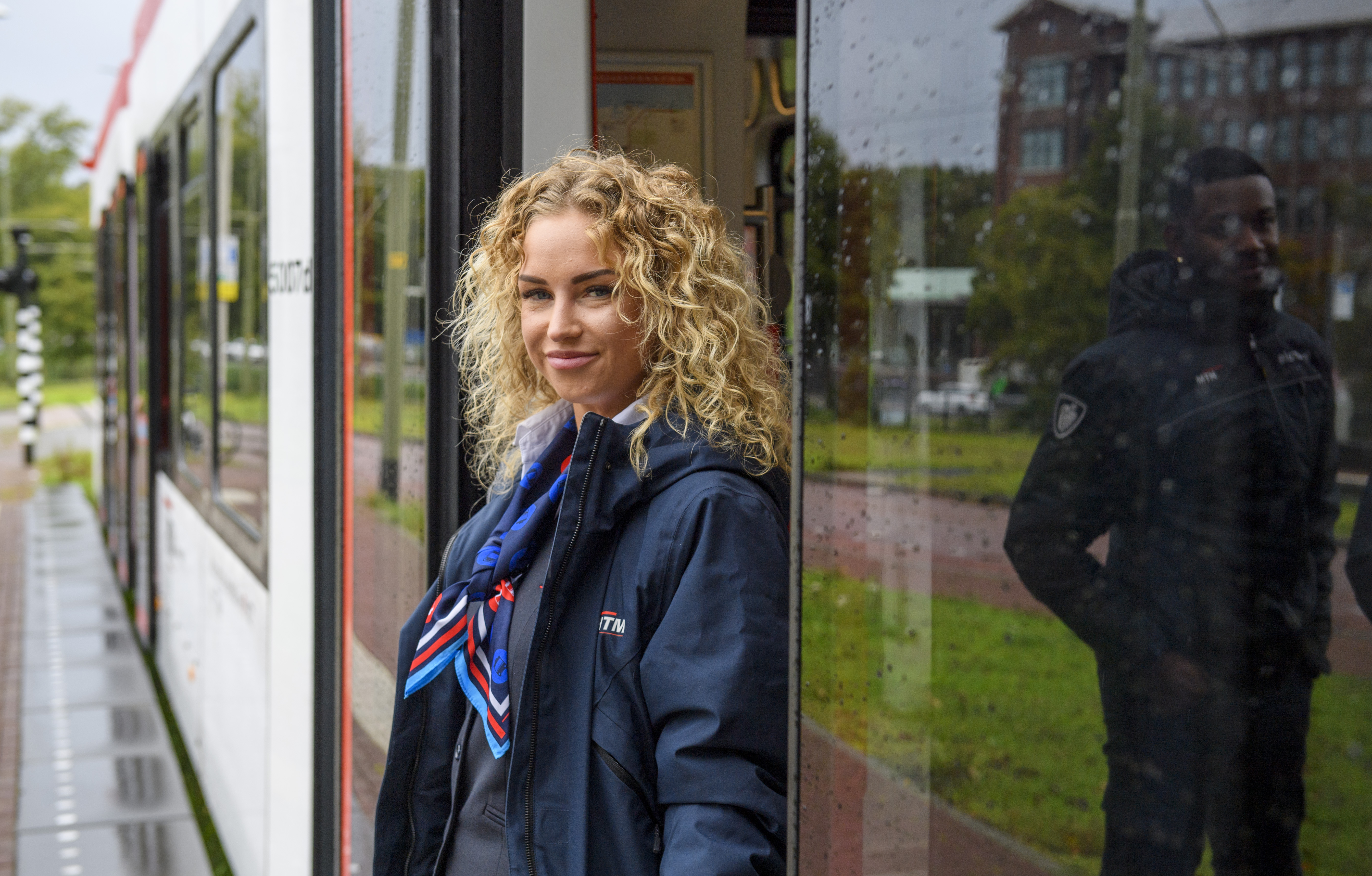 HTM boa staat in deuropening HTM tram en lacht naar de camera