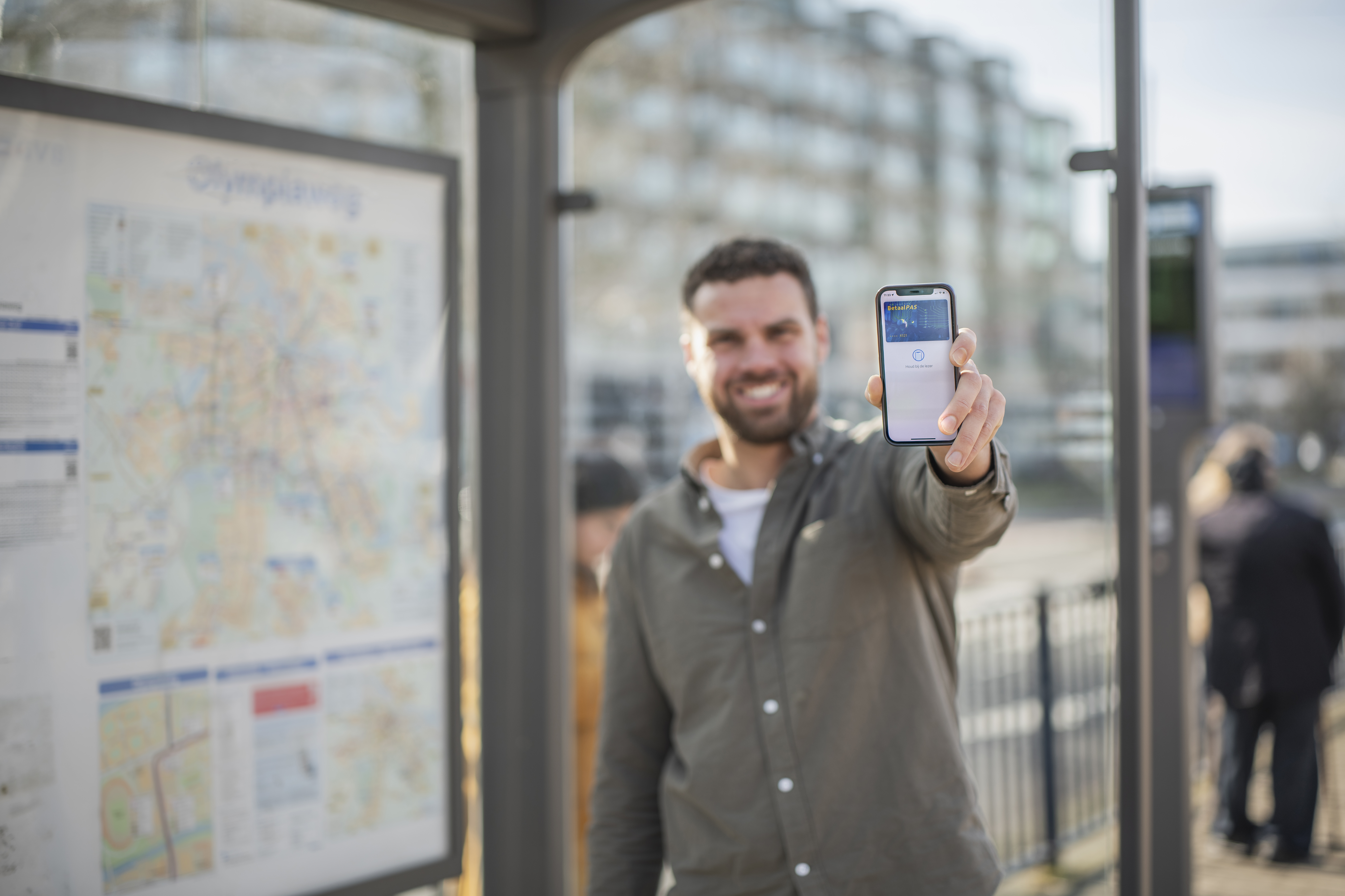 Man in bushokje die zijn mobile telefoon laat zien met daarop zijn betaalpas