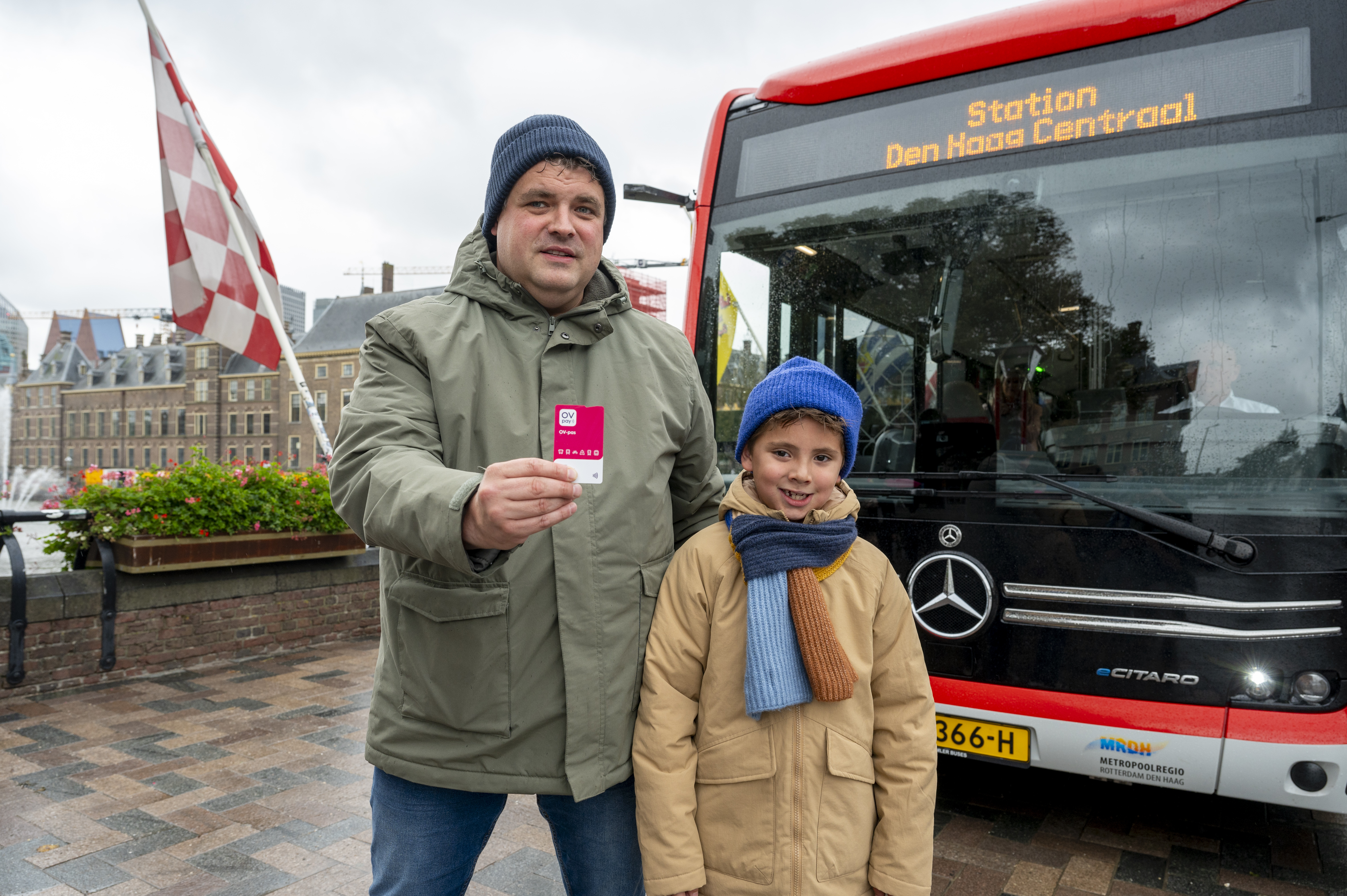 Vader en zoon staan voor een HTM bus met de nieuwe OV-pas in hun handen