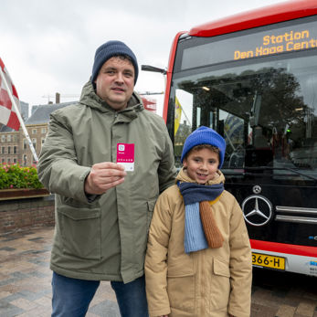 Vader en zoon staan voor een HTM bus met de nieuwe OV-pas in hun handen Vader en zoon staan voor een HTM bus met de nieuwe OV-pas in hun handen
