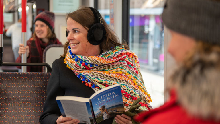 Vrouw leest boek in HTM tram en heeft oorwarmers op Vrouw leest boek in HTM tram en heeft oorwarmers op