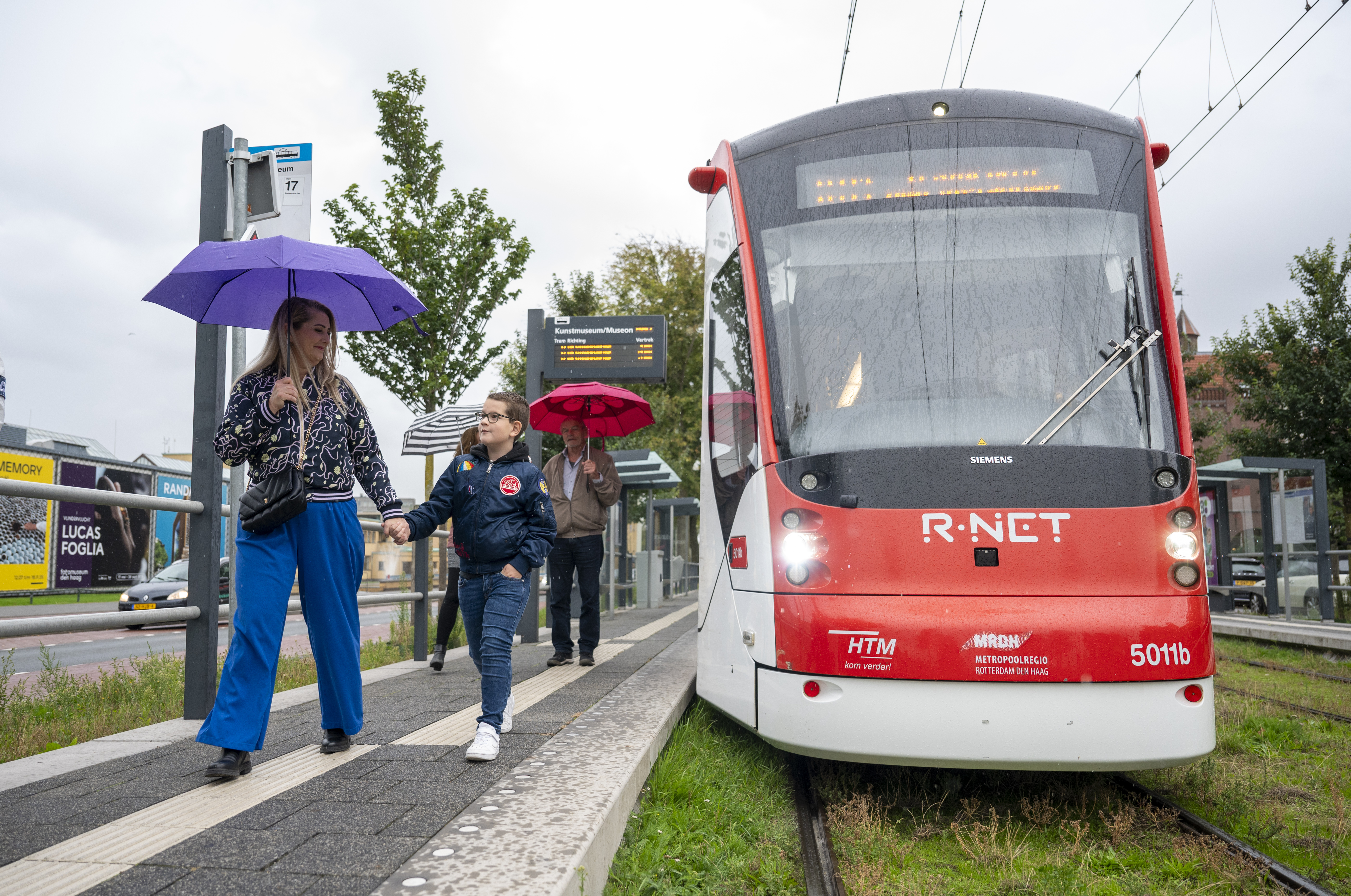 Moeder en zoon lopen in de regen op een tramhalte
