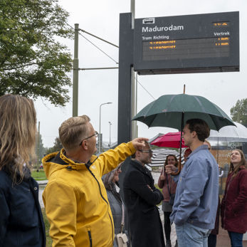 Reizigers op een halte met op de achtergrond een digitaal reisinformatiebord Reizigers op een halte met op de achtergrond een digitaal reisinformatiebord