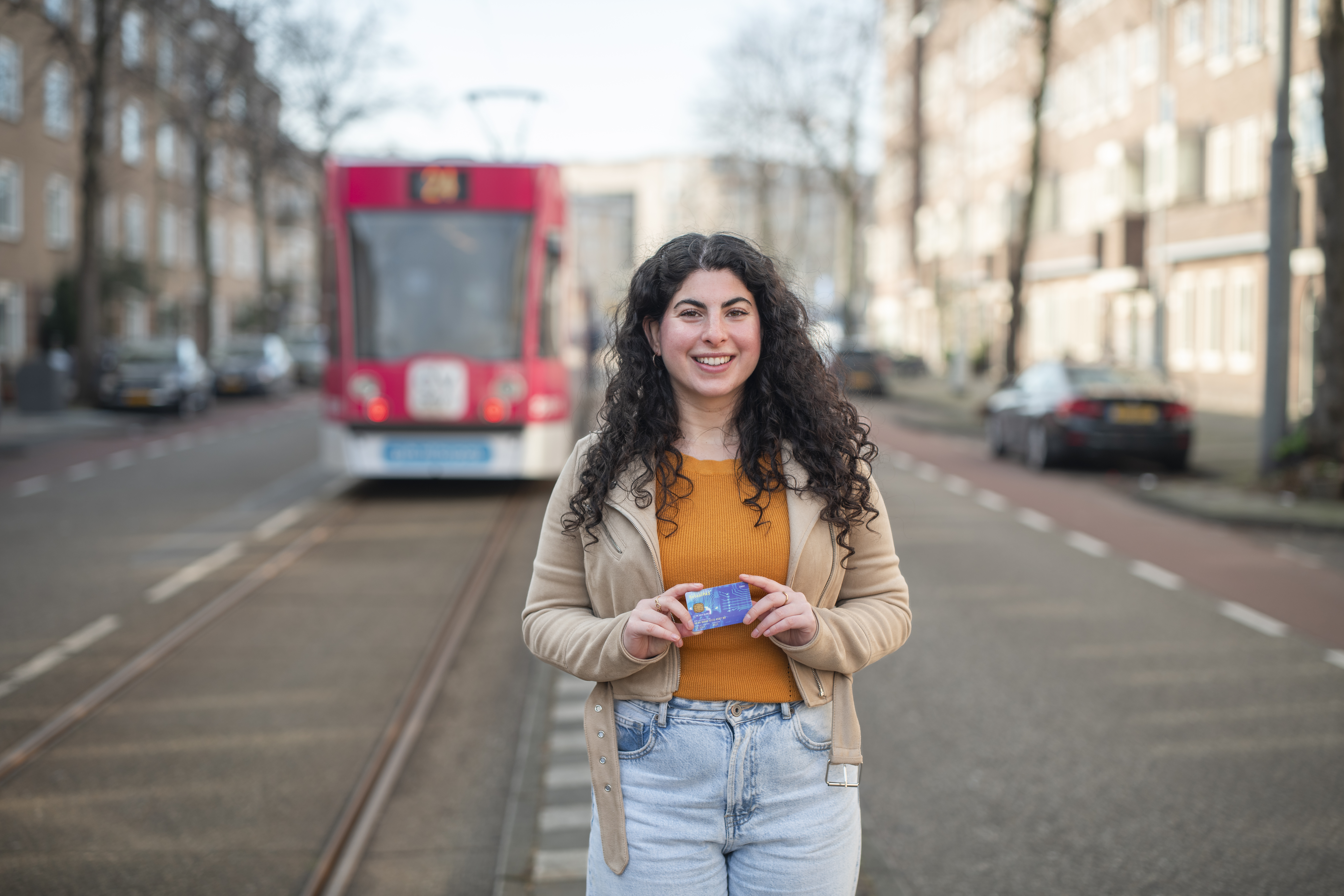 Vrouw met donkere krullen met betaalpas in haar hand poseert voor tram