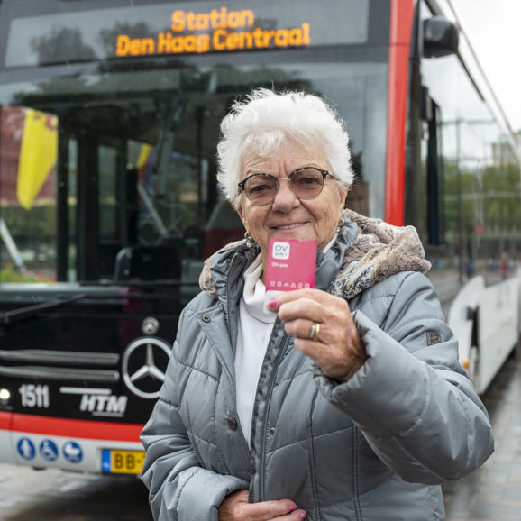 Oude vrouw met bril staat voor een HTM bus met een nieuwe roze OV-pas in haar hand Oude vrouw met bril staat voor een HTM bus met een nieuwe roze OV-pas in haar hand